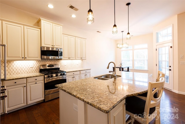 kitchen featuring appliances with stainless steel finishes, decorative light fixtures, and a center island with sink