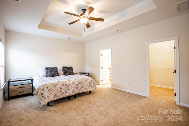 carpeted bedroom with ceiling fan, a walk in closet, crown molding, and a tray ceiling