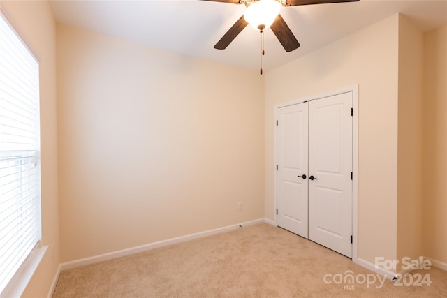 unfurnished bedroom featuring a closet, light colored carpet, and ceiling fan