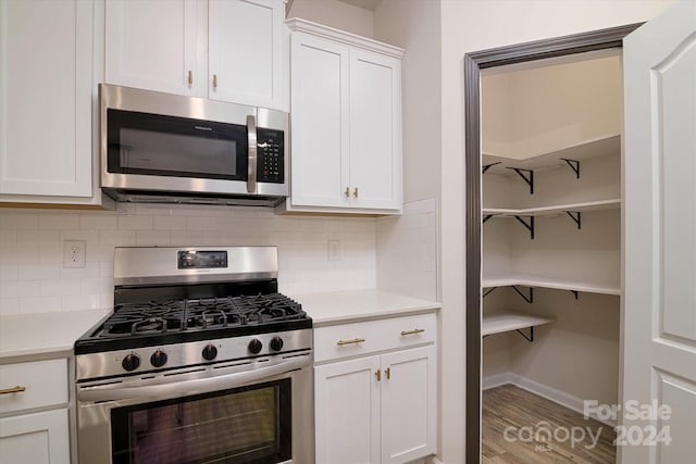 kitchen featuring backsplash, stainless steel appliances, white cabinetry, and hardwood / wood-style flooring