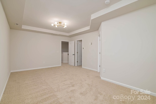 carpeted empty room with a notable chandelier and a tray ceiling