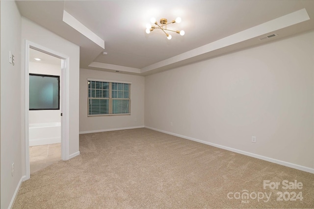 unfurnished room featuring a notable chandelier, light colored carpet, and a tray ceiling