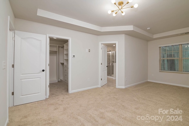 unfurnished bedroom with light carpet, a closet, a walk in closet, a tray ceiling, and a chandelier