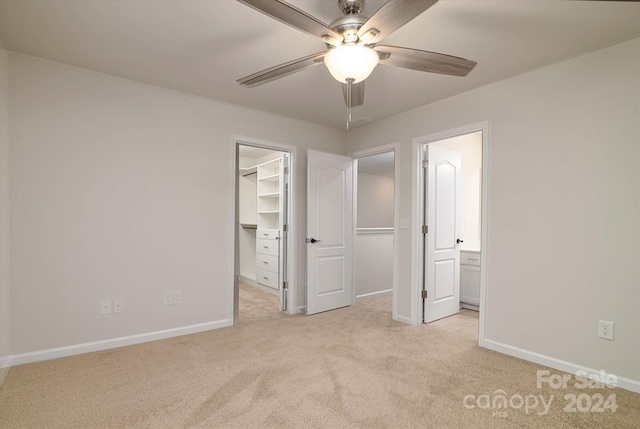 unfurnished bedroom with ensuite bathroom, light colored carpet, ceiling fan, a spacious closet, and a closet