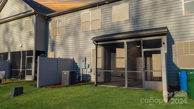 back house at dusk featuring a sunroom, a lawn, and central air condition unit