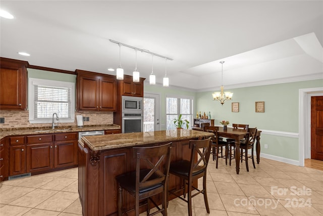 kitchen with sink, light stone counters, pendant lighting, a kitchen island, and appliances with stainless steel finishes