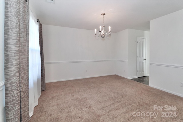 carpeted empty room featuring a chandelier