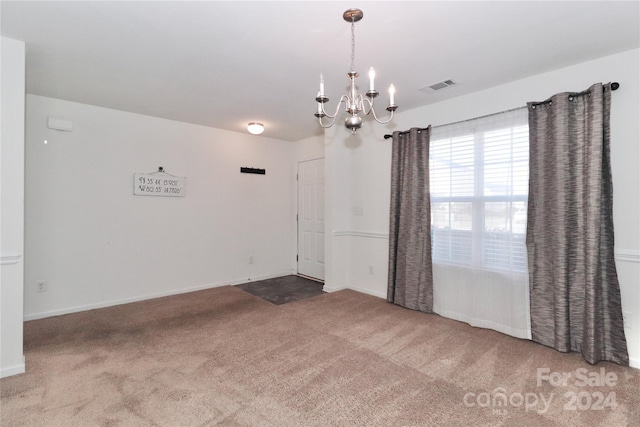 spare room featuring carpet and a chandelier