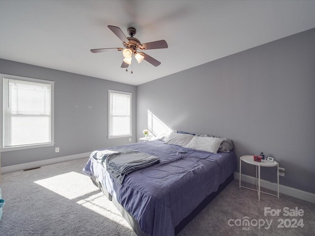 bedroom with multiple windows, dark colored carpet, and ceiling fan