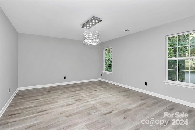 spare room featuring a healthy amount of sunlight, a notable chandelier, and light hardwood / wood-style floors