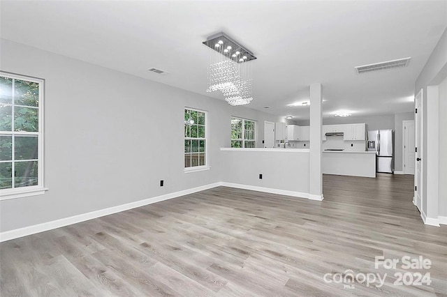 unfurnished living room featuring a notable chandelier and light hardwood / wood-style flooring