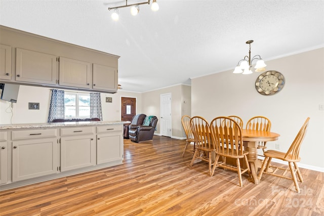 dining space featuring a textured ceiling, ornamental molding, a notable chandelier, and light wood-type flooring