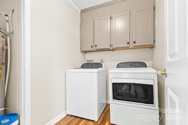 laundry room featuring cabinets, ornamental molding, a textured ceiling, washer and clothes dryer, and light hardwood / wood-style floors