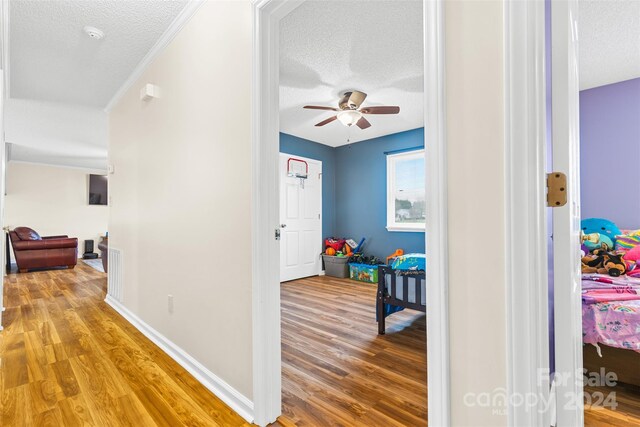 corridor featuring hardwood / wood-style floors, a textured ceiling, and ornamental molding