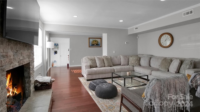 living room with dark hardwood / wood-style floors, a stone fireplace, and crown molding