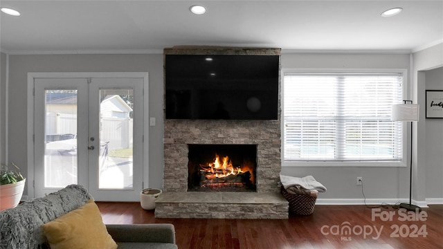 living room featuring hardwood / wood-style flooring, a stone fireplace, ornamental molding, and french doors