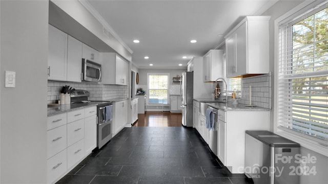 kitchen featuring a healthy amount of sunlight, light stone countertops, white cabinetry, and stainless steel appliances