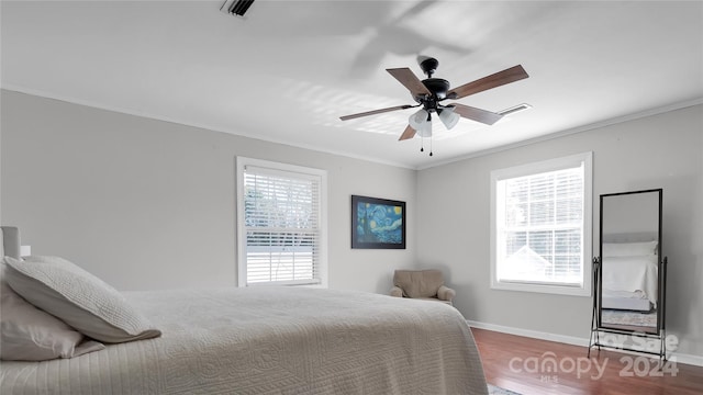 bedroom featuring ceiling fan, wood-type flooring, crown molding, and multiple windows