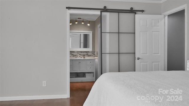 bedroom featuring ensuite bathroom, track lighting, ornamental molding, a barn door, and dark hardwood / wood-style floors