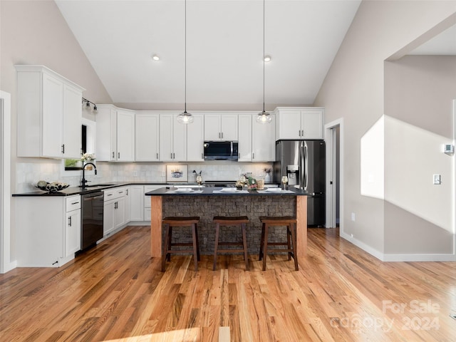 kitchen featuring pendant lighting, backsplash, white cabinets, light hardwood / wood-style floors, and stainless steel appliances