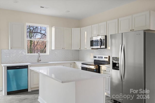 kitchen with backsplash, stainless steel appliances, sink, white cabinets, and a center island