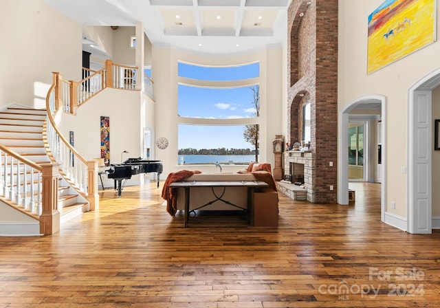 entrance foyer featuring beam ceiling, coffered ceiling, a high ceiling, a stone fireplace, and wood-type flooring