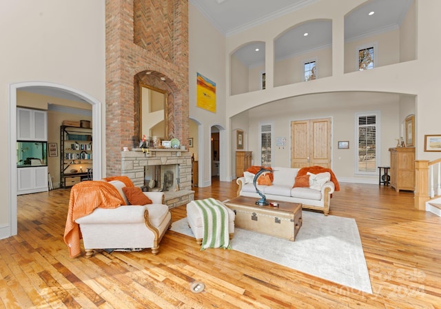 living room featuring a stone fireplace, light wood-type flooring, a towering ceiling, and crown molding