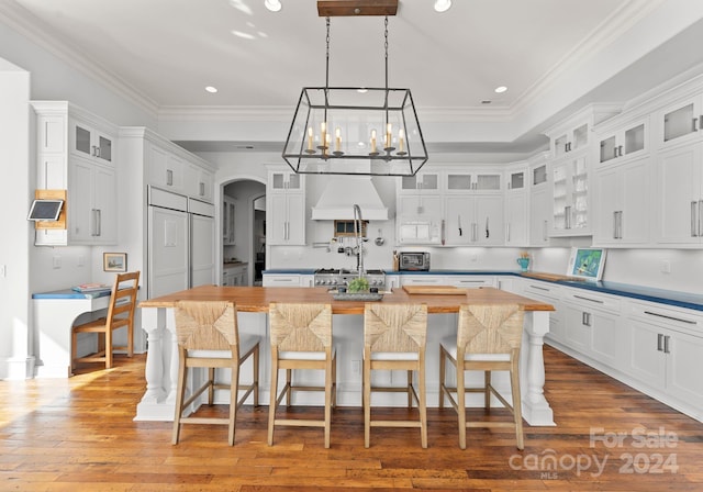 kitchen with a kitchen breakfast bar, wood-type flooring, a kitchen island with sink, white cabinets, and custom exhaust hood