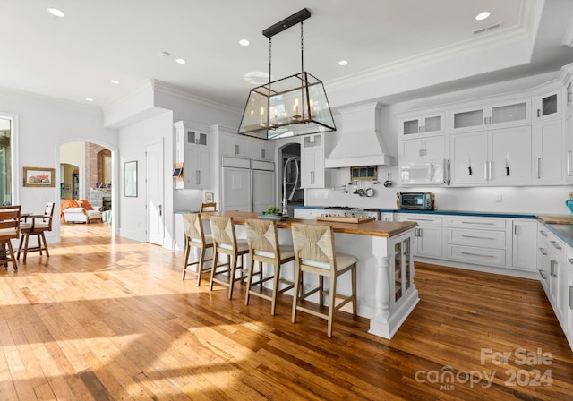 kitchen with white cabinetry, hardwood / wood-style floors, a kitchen island, and custom exhaust hood