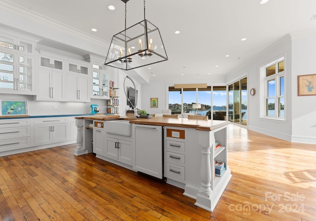 kitchen with white cabinetry, wooden counters, an island with sink, white dishwasher, and light hardwood / wood-style floors