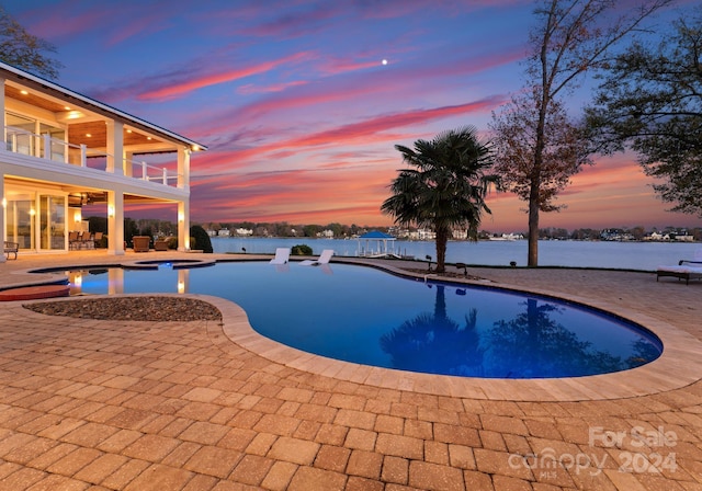 pool at dusk featuring a patio area, a jacuzzi, and a water view