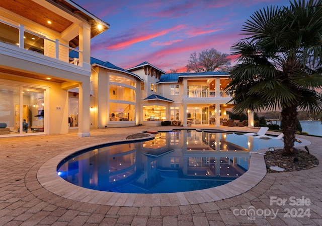 pool at dusk featuring a patio and a hot tub