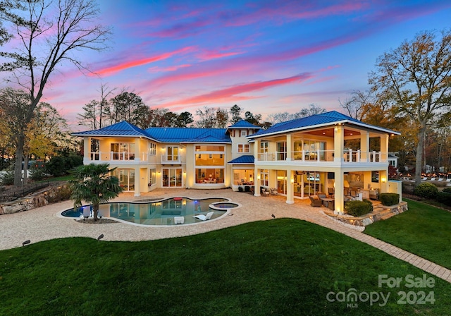 back house at dusk with an outdoor hangout area, a balcony, a swimming pool with hot tub, a yard, and a patio