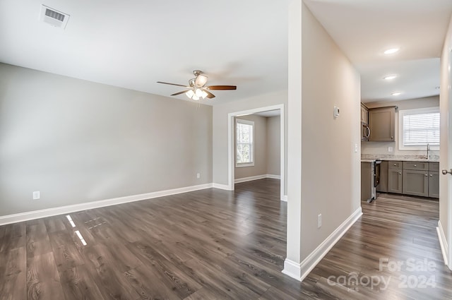 unfurnished living room featuring ceiling fan, a healthy amount of sunlight, sink, and dark wood-type flooring