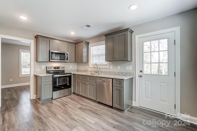 kitchen featuring light stone countertops, appliances with stainless steel finishes, light hardwood / wood-style flooring, and gray cabinetry