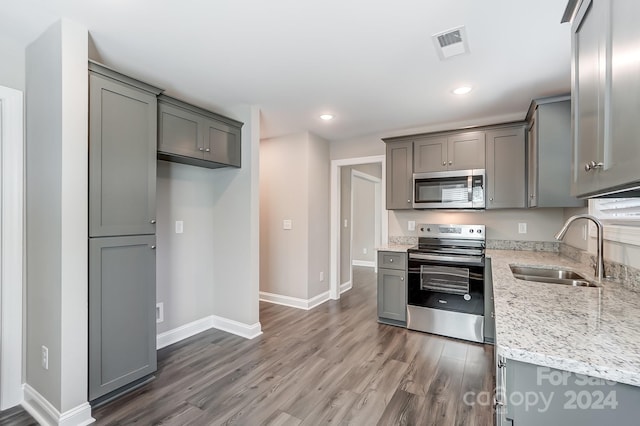 kitchen with sink, stainless steel appliances, light stone counters, dark hardwood / wood-style floors, and gray cabinets