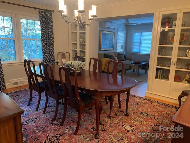 dining room featuring hardwood / wood-style floors, ceiling fan with notable chandelier, a wall mounted AC, and crown molding