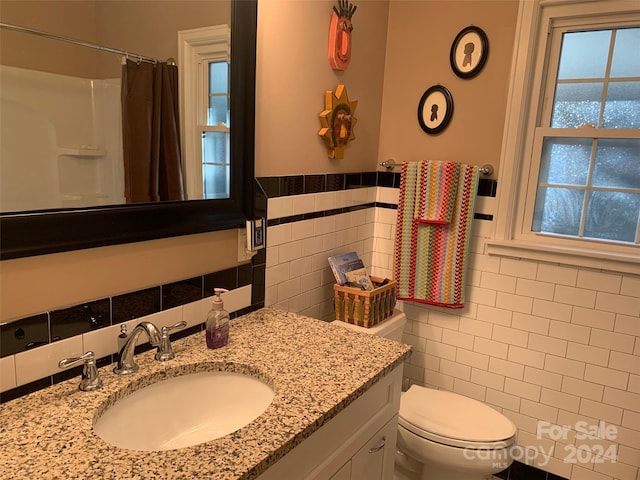 bathroom featuring vanity, toilet, tile walls, and walk in shower