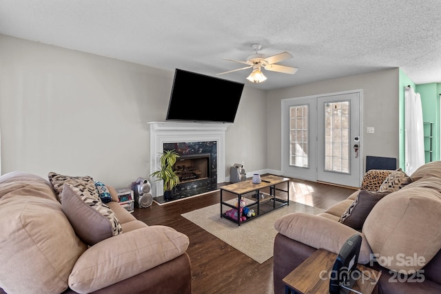 living room with ceiling fan, dark wood-type flooring, a premium fireplace, and a textured ceiling