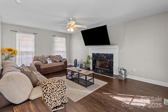 living room featuring dark wood-type flooring, ceiling fan, and a premium fireplace