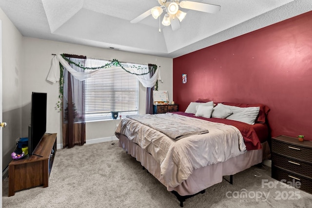 bedroom with a textured ceiling, light colored carpet, a raised ceiling, and ceiling fan