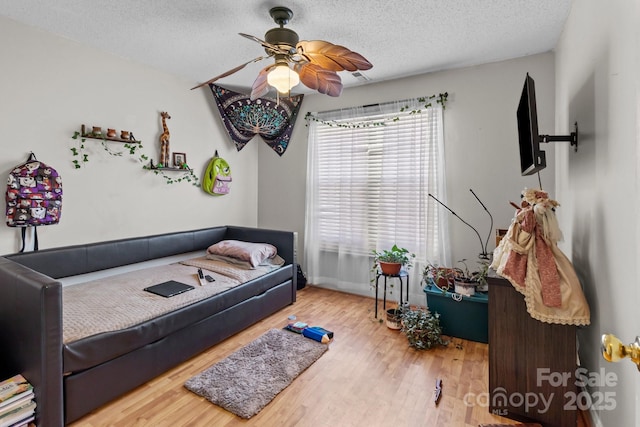 bedroom with ceiling fan, light hardwood / wood-style floors, and a textured ceiling