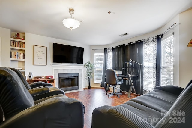 living room featuring built in features, wood-type flooring, and a tile fireplace