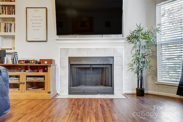 details with a tiled fireplace, hardwood / wood-style floors, and built in shelves