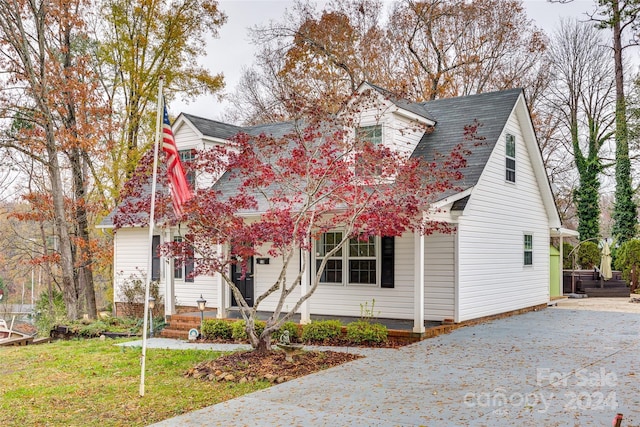 new england style home featuring covered porch and a front lawn