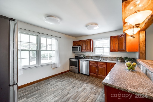 kitchen with light stone countertops, sink, light wood-type flooring, and stainless steel appliances