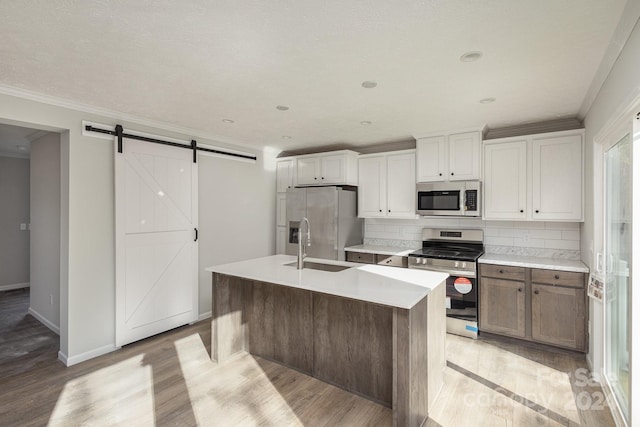 kitchen featuring a kitchen island with sink, a barn door, appliances with stainless steel finishes, light hardwood / wood-style floors, and white cabinetry