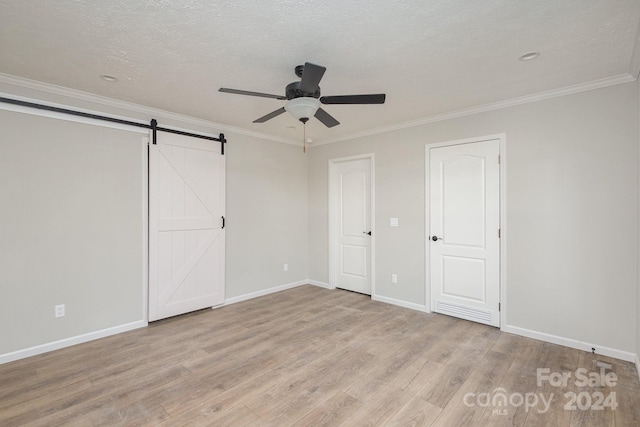 unfurnished bedroom featuring ceiling fan, a barn door, crown molding, light hardwood / wood-style floors, and a textured ceiling