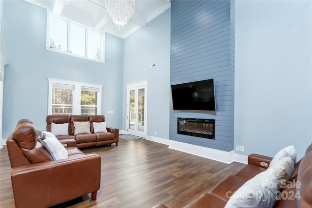 living room featuring hardwood / wood-style floors, a high ceiling, ornamental molding, a notable chandelier, and a large fireplace