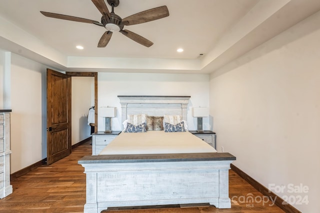 bedroom with dark hardwood / wood-style floors, ceiling fan, and a raised ceiling